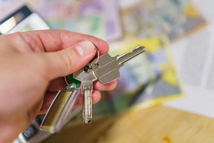 Hand holding a set of keys with blurred cash in the background