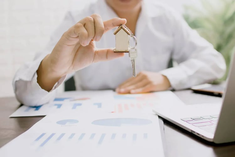 Hands holding a small house-shaped charm above financial paperwork