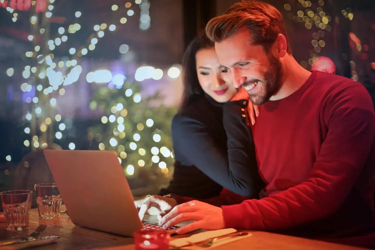 Couple smiling at a laptop at a table with string lights