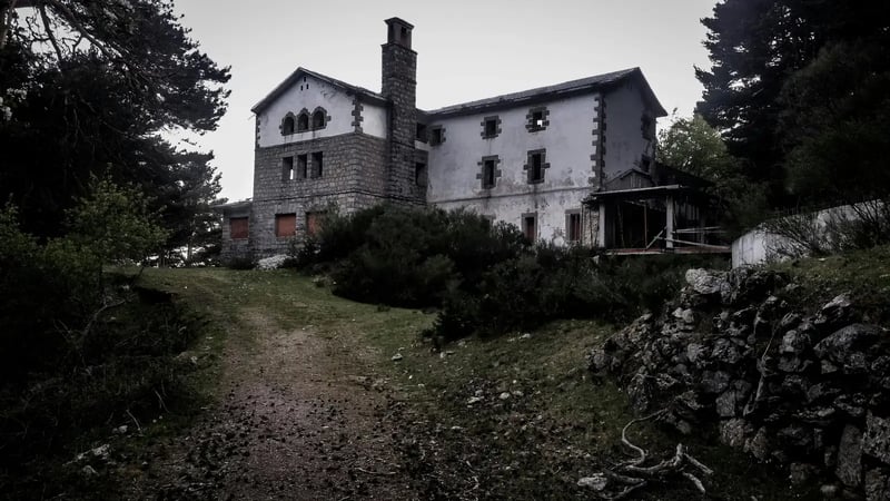 Old abandoned stone house among trees at the end of an overgrown path