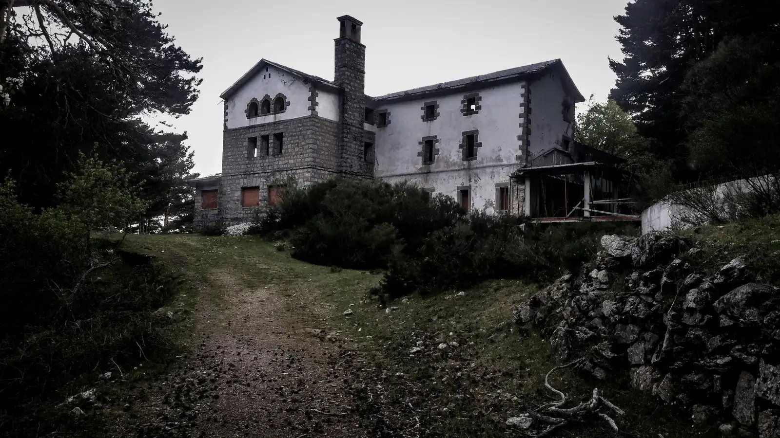 Old abandoned stone house among trees at the end of an overgrown path