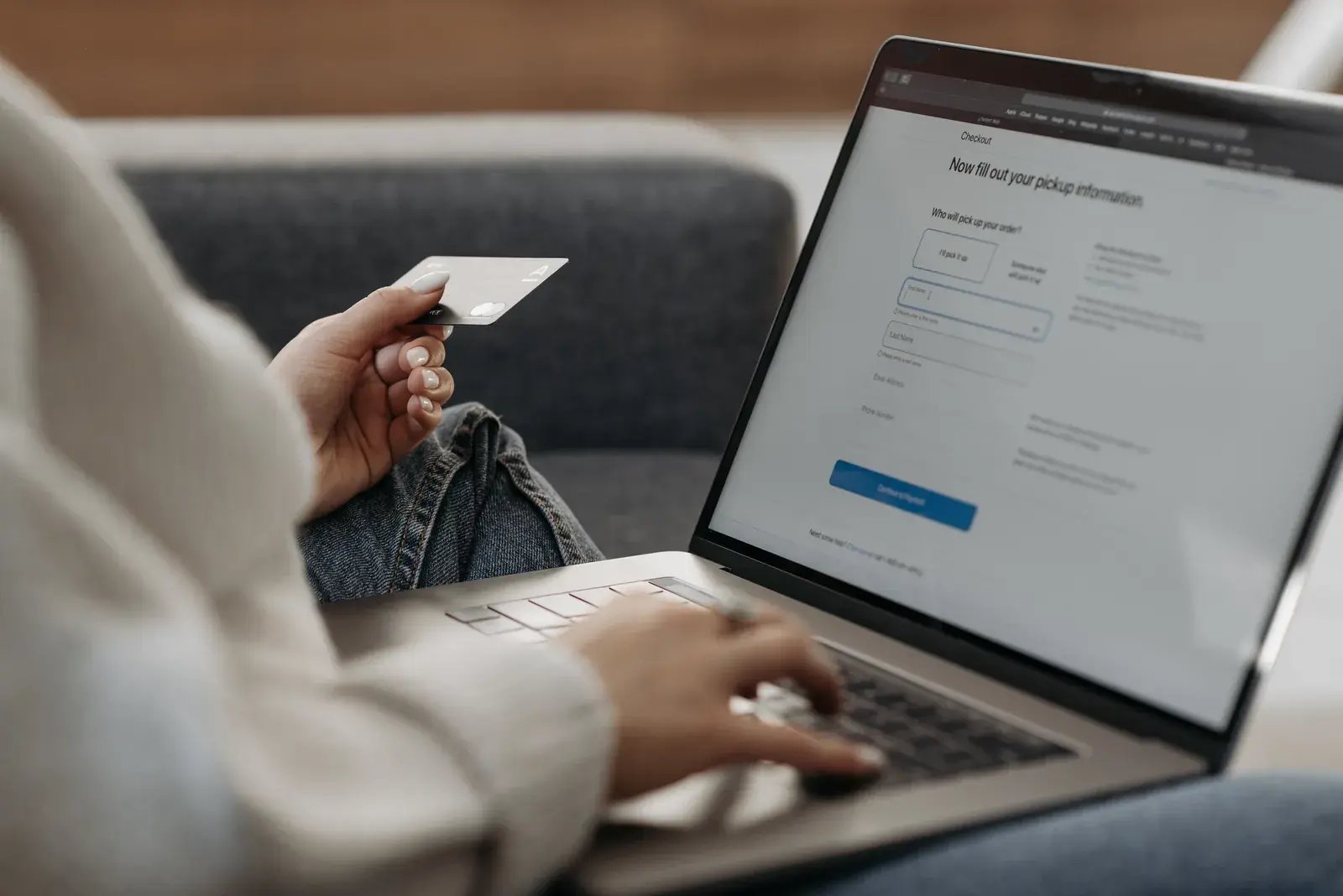 Person holding a card while typing on a laptop on a couch