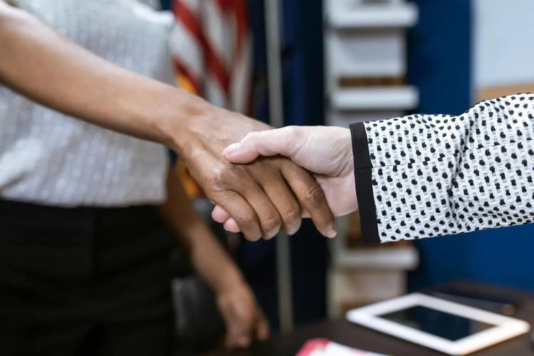 Two people shaking hands over a desk with documents and a phone