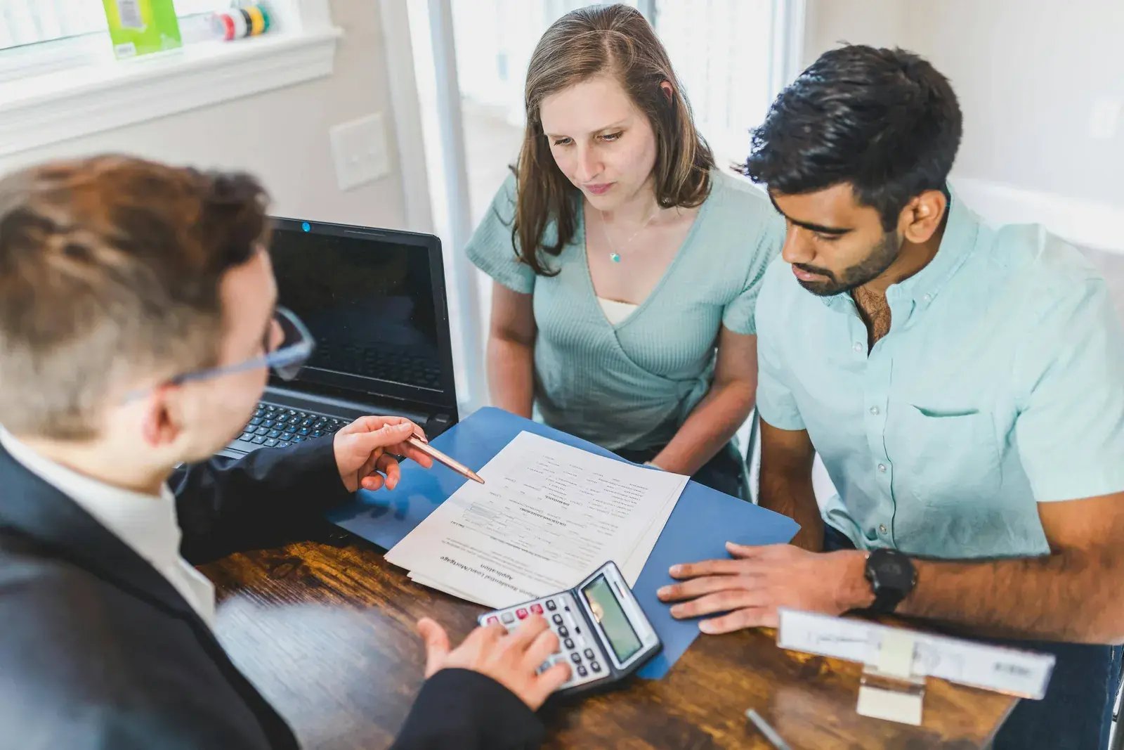 Three people reviewing documents and a tablet at a conference table