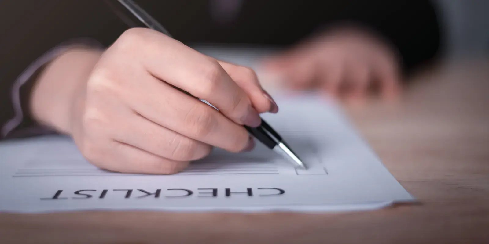 Hand holding a pen over a paper checklist