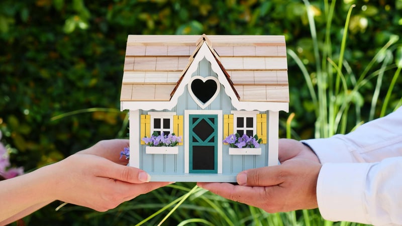 Small model house being handed from one person to another outdoors