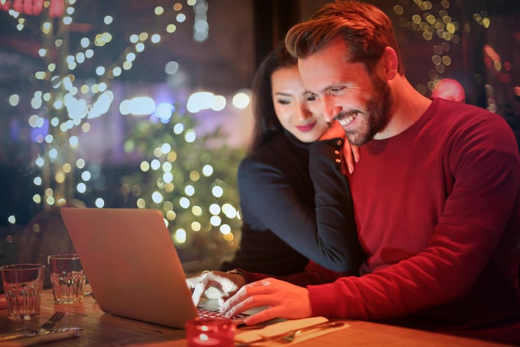 Couple smiling at a laptop at a table with string lights