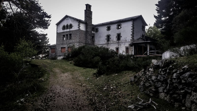 Old abandoned stone house among trees at the end of an overgrown path