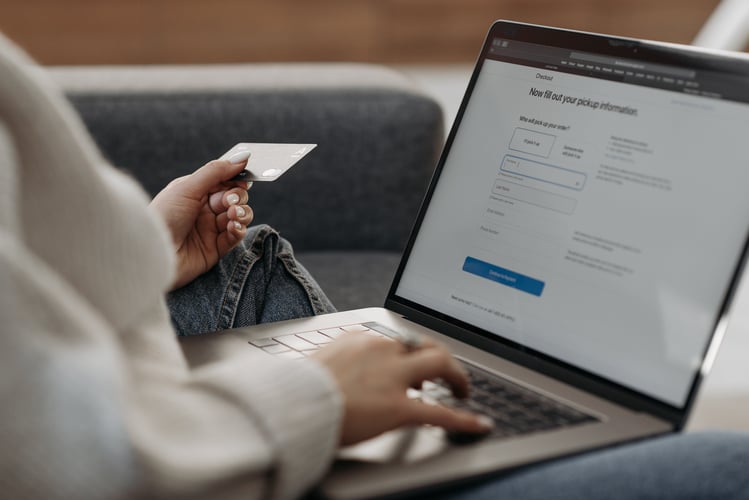 Person holding a card while typing on a laptop on a couch