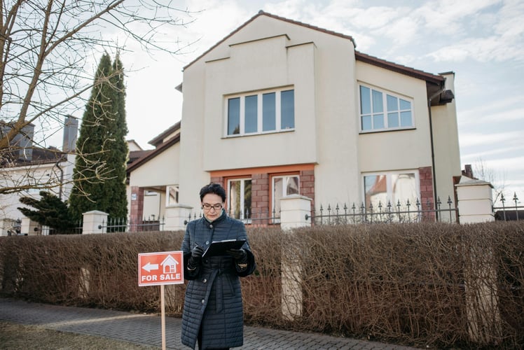 Person standing near a small For Sale sign in front of a white house