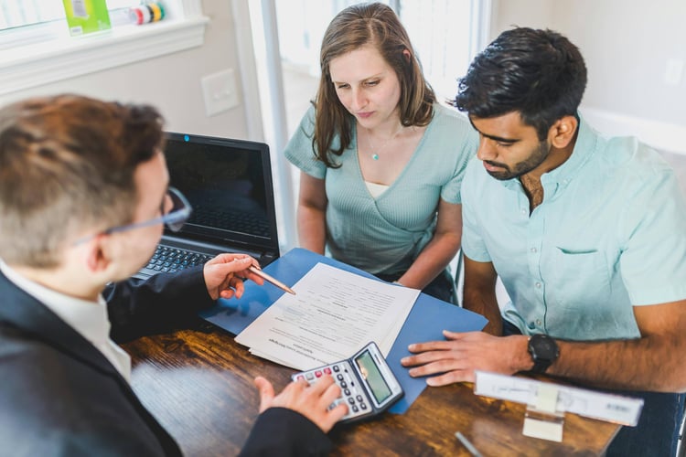 Three people reviewing documents and a tablet at a conference table